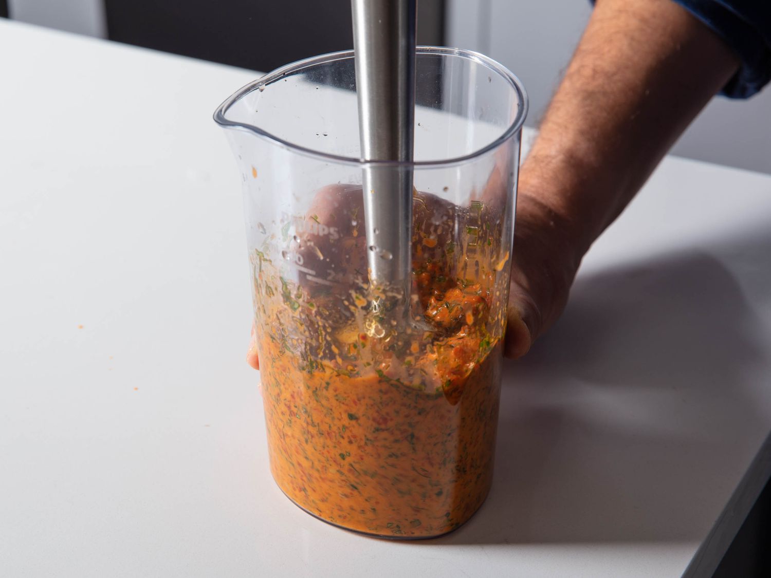 A stick blender purees the roasted red pepper with herbs and other ingredients.