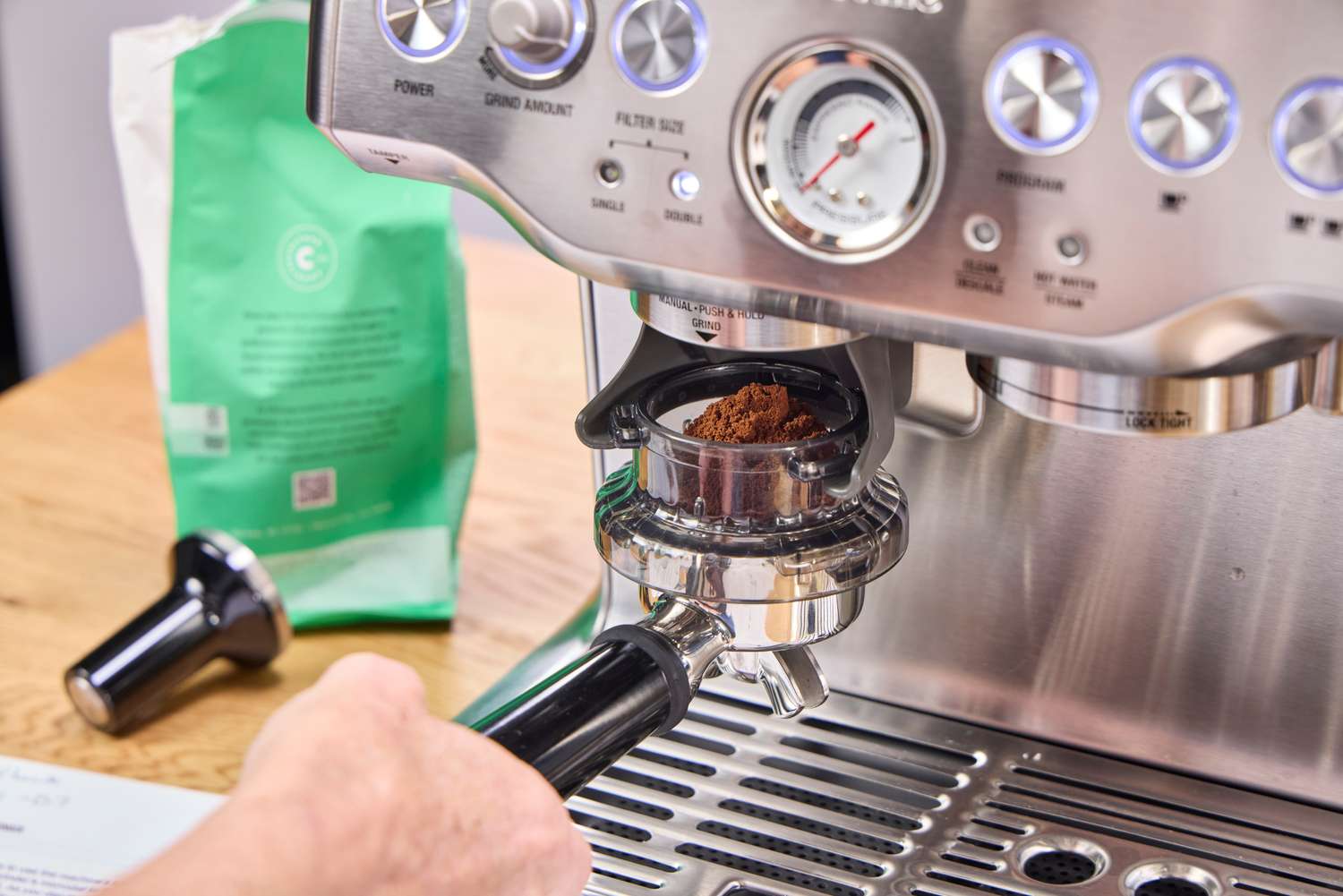 A person adds ground espresso beans to the Breville The Barista Express Espresso Machine