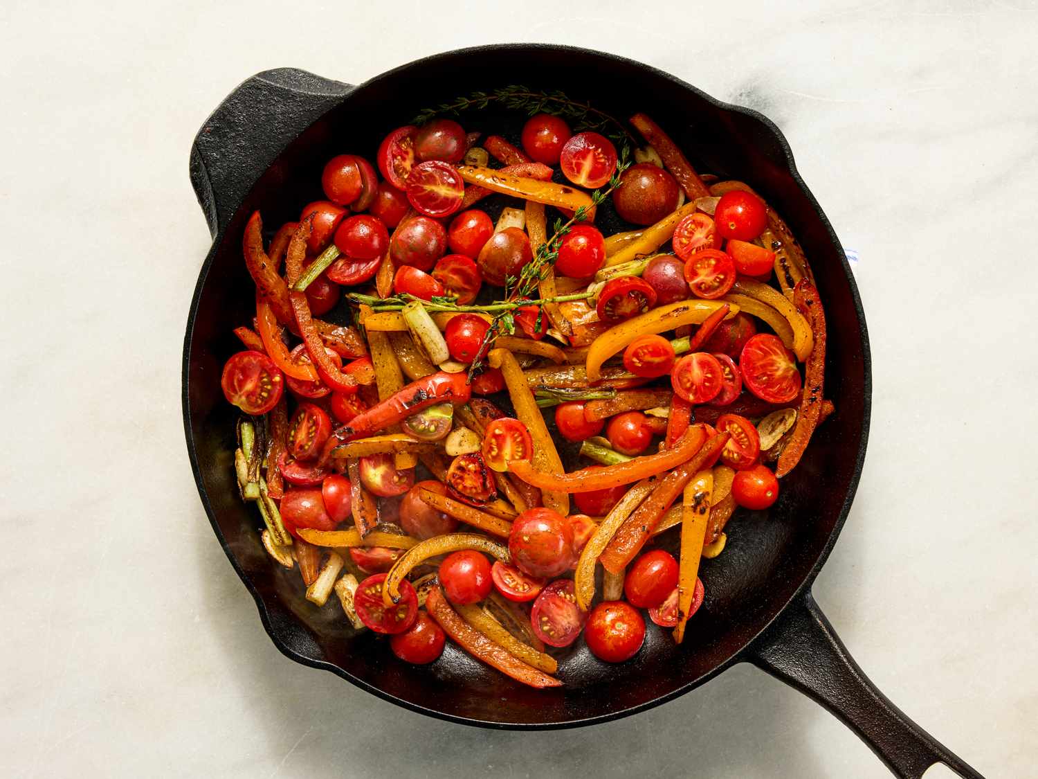 Sauted vegetables including cherry tomatoes and bell peppers in a cast iron skillet