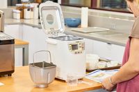 A person reading instructions in front of an opened Zojirushi Home Bakery Mini Breadmaker and basket