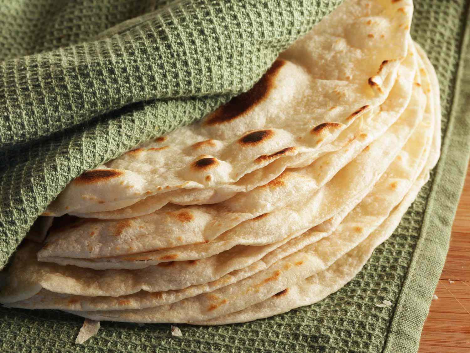 A stack of cook-and-serve flour tortillas wrapped in a green kitchen towel. 