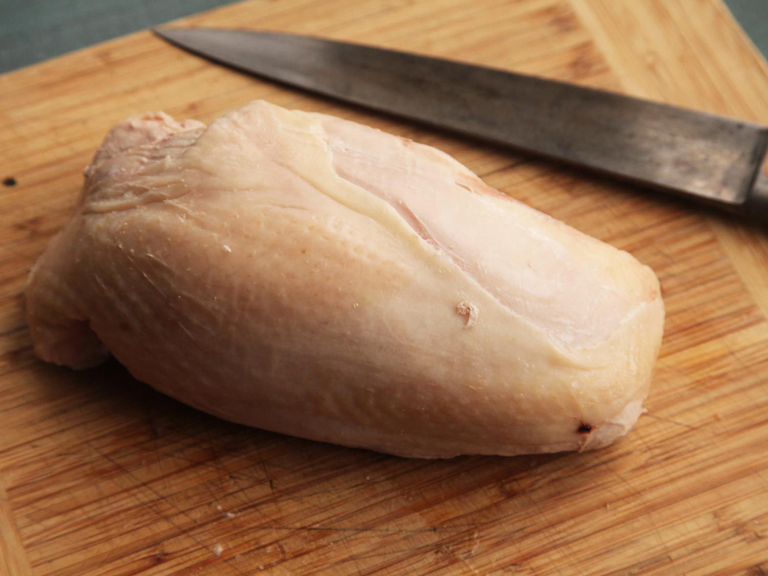 Skin-on sous vide turkey breast on a wooden cutting board with knife in the background.