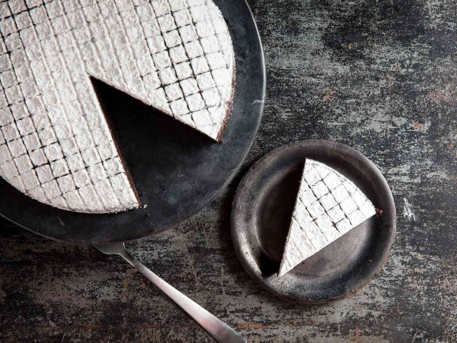 Overhead view of dairy-free chocolate cake dusted with powdered sugar and served on slate-colored plates.