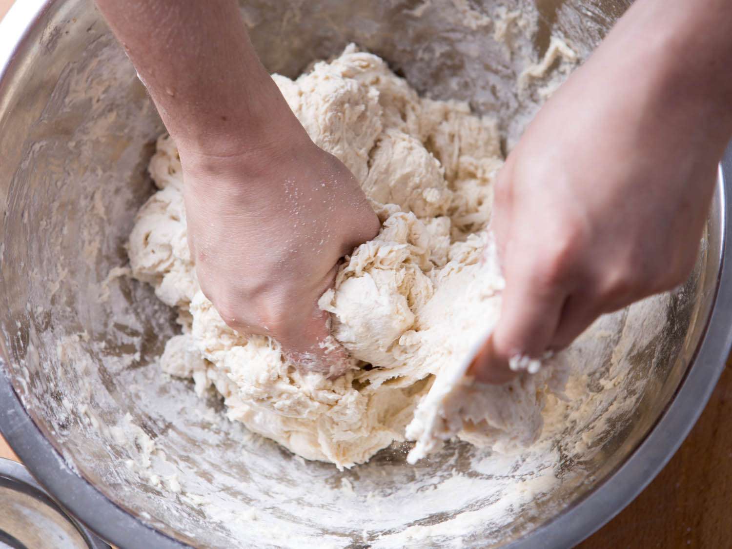 Hands kneading bread dough in a mixing bowl.