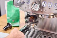 A person adds ground espresso beans to the Breville The Barista Express Espresso Machine