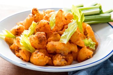 A plate of crispy buffalo fried cauliflower, with celery sticks on the side of the plate.