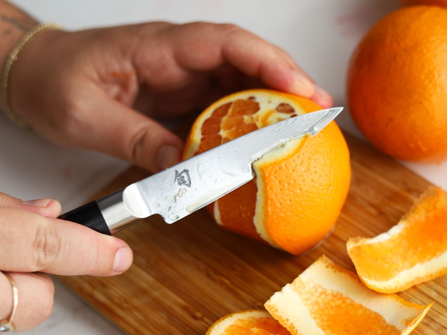 A person using a paring knife to cut away an orange's peel.