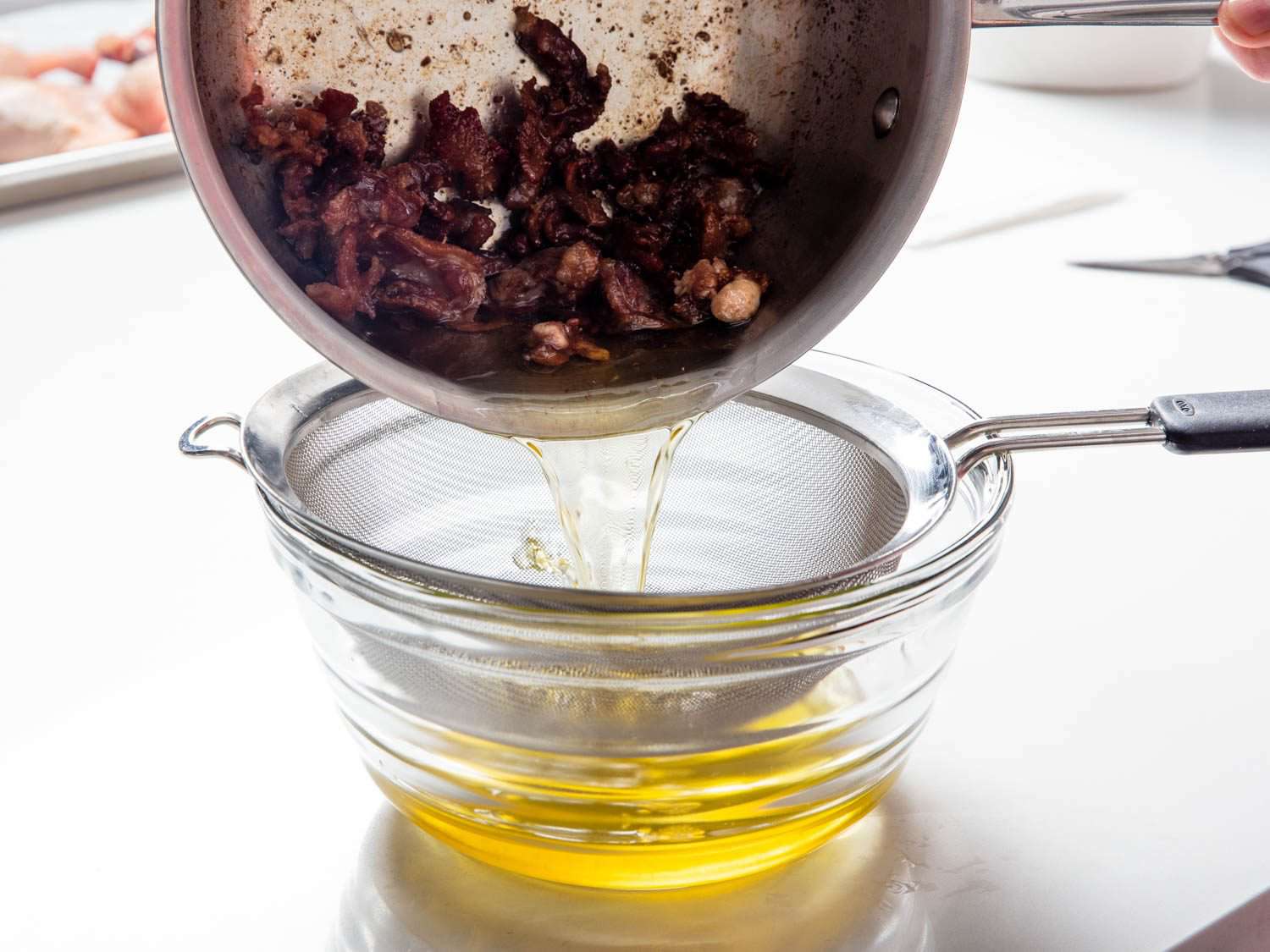 Straining duck fat into a heatproof bowl through a fine-mesh strainer.