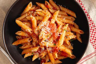 A bowl of penne pasta topped with tomato sauce and grated cheese
