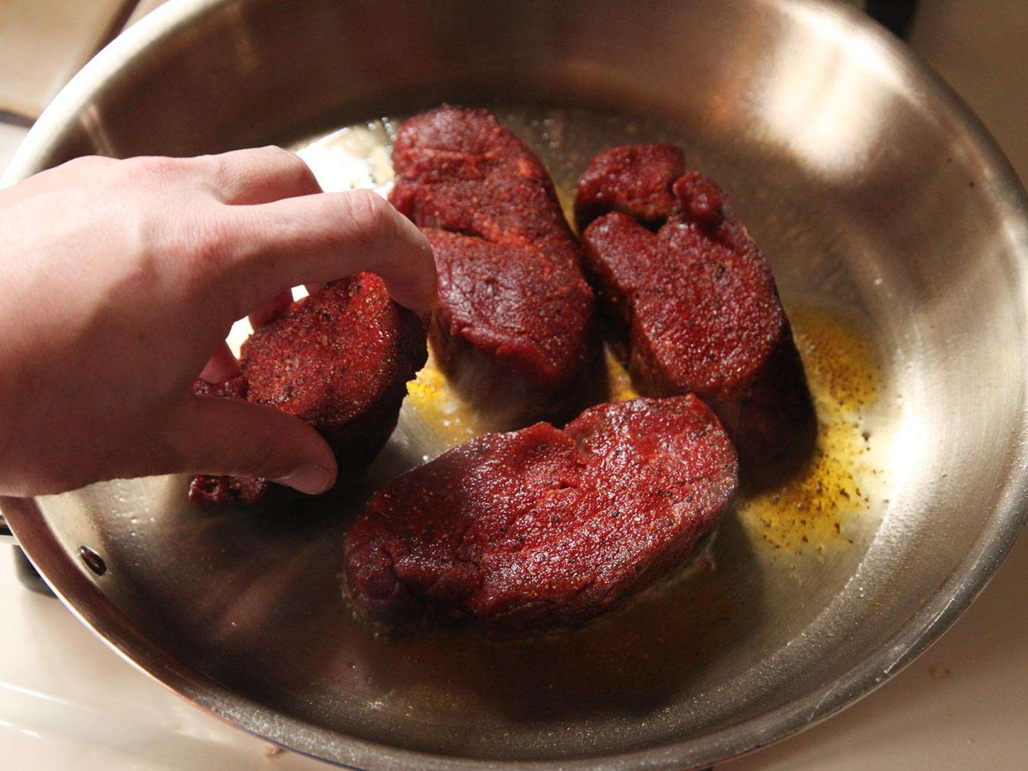 Four steaks searing in a skillet.