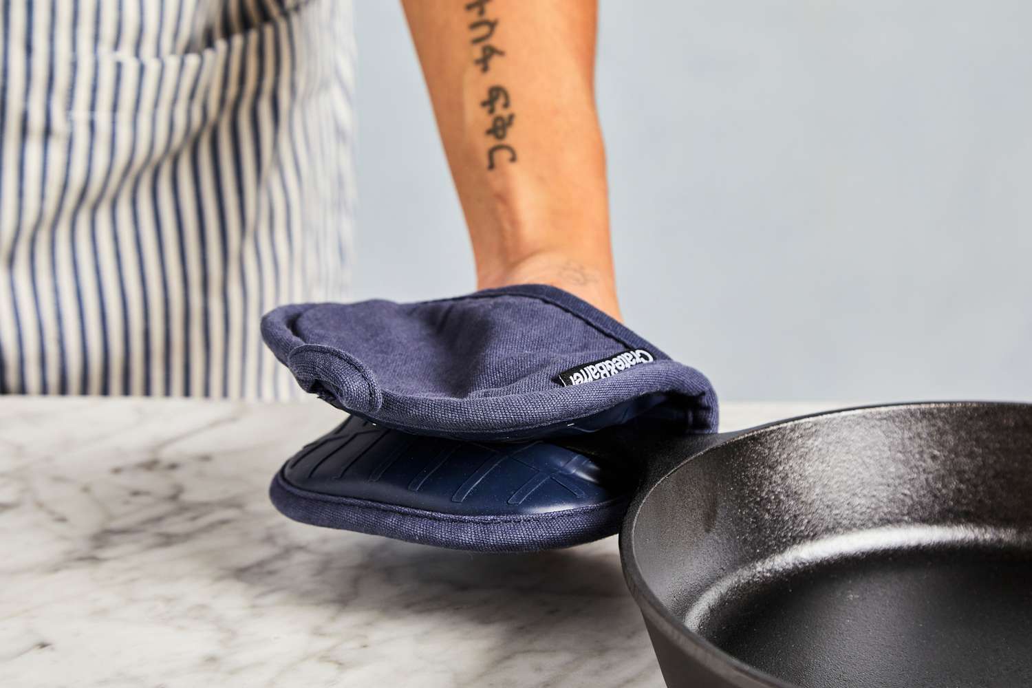 a person using the crate and barrel pot holder to grab the handle on a cast iron skillet
