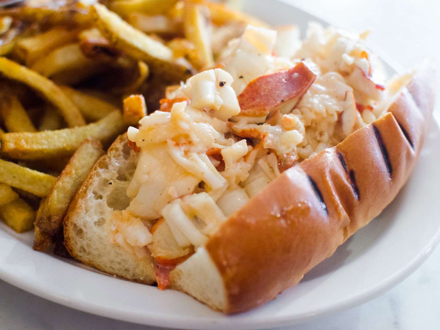 A hot buttered lobster roll on a plate with fries from Neptune Oyster in Boston.