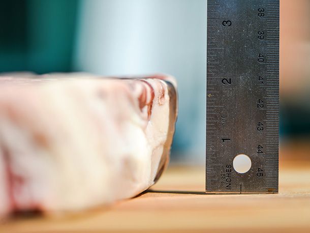 Profile shot of the steak on a cutting board. Author is measuring its thickness with a ruler. The measurement reads two inches. 