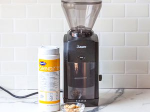 A coffee grinder and a bottle of coffee grinder cleaner on a wooden countertop.