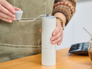 A person turns the crank on the top of the Timemore C2 Max Manual Grinder