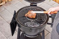 A person flips meat cooked in the Char-Griller E16620 Akorn Kamado Charcoal Grill