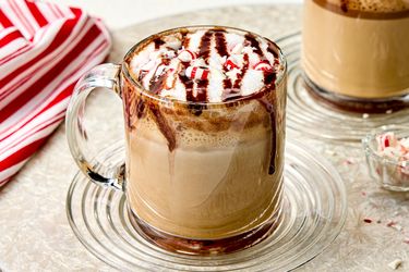 A mug of coffee topped with whipped cream chocolate drizzle and crushed peppermint candy