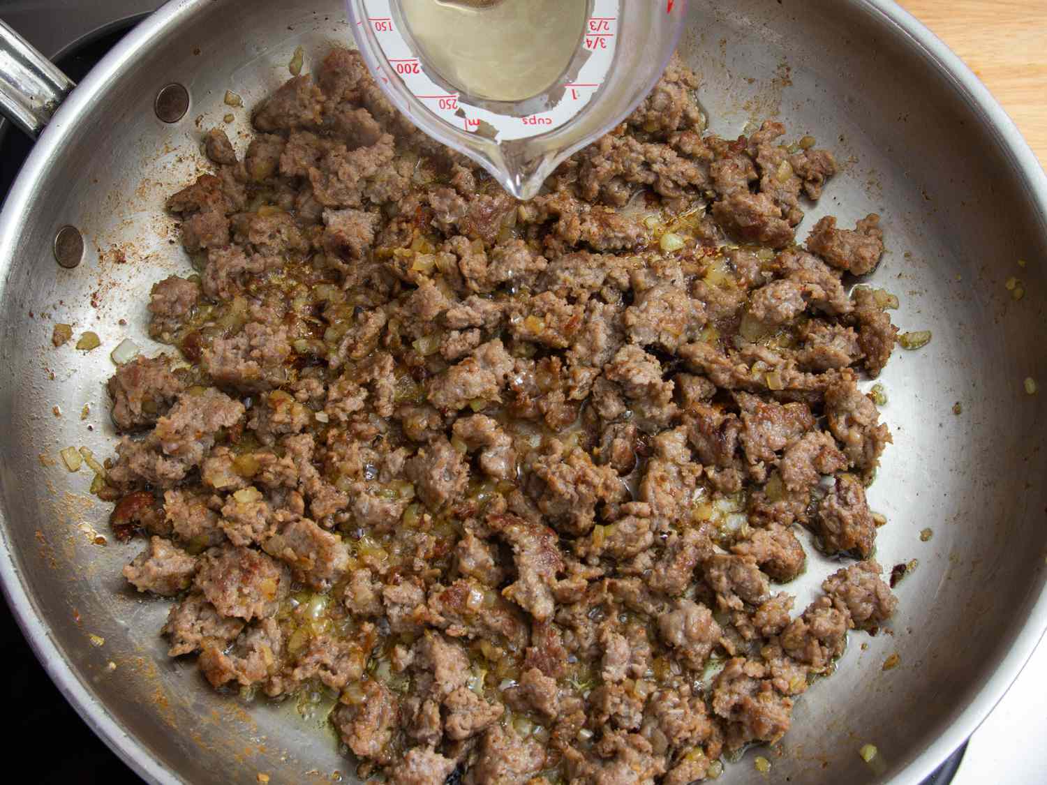 Overhead view of wine being poured into the cooked sausage mixture.