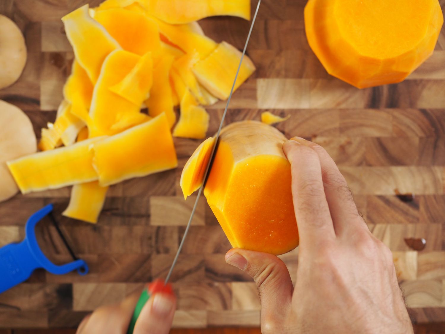 A slicing knife trimming the skin from the neck of a butternut squash.