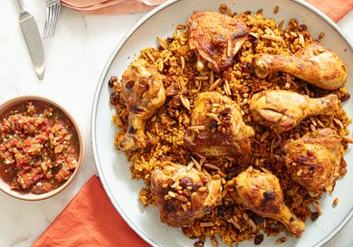 A plate containing a dish of chicken drumsticks served over seasoned rice with a bowl of sauce on the side