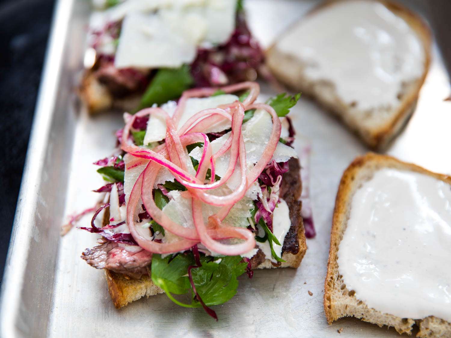 Pickled red onion on top of an open face steak sandwich.