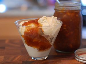 A conical glass containing whiskey peach sauce served over vanilla ice cream.
