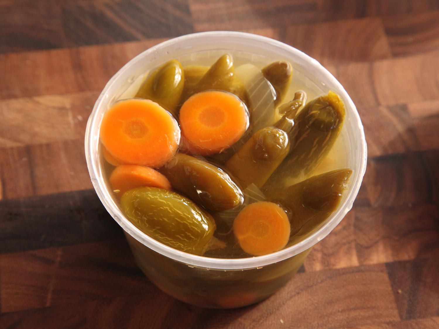 Plastic container full of pickled jalapeños and sliced carrot in brine.