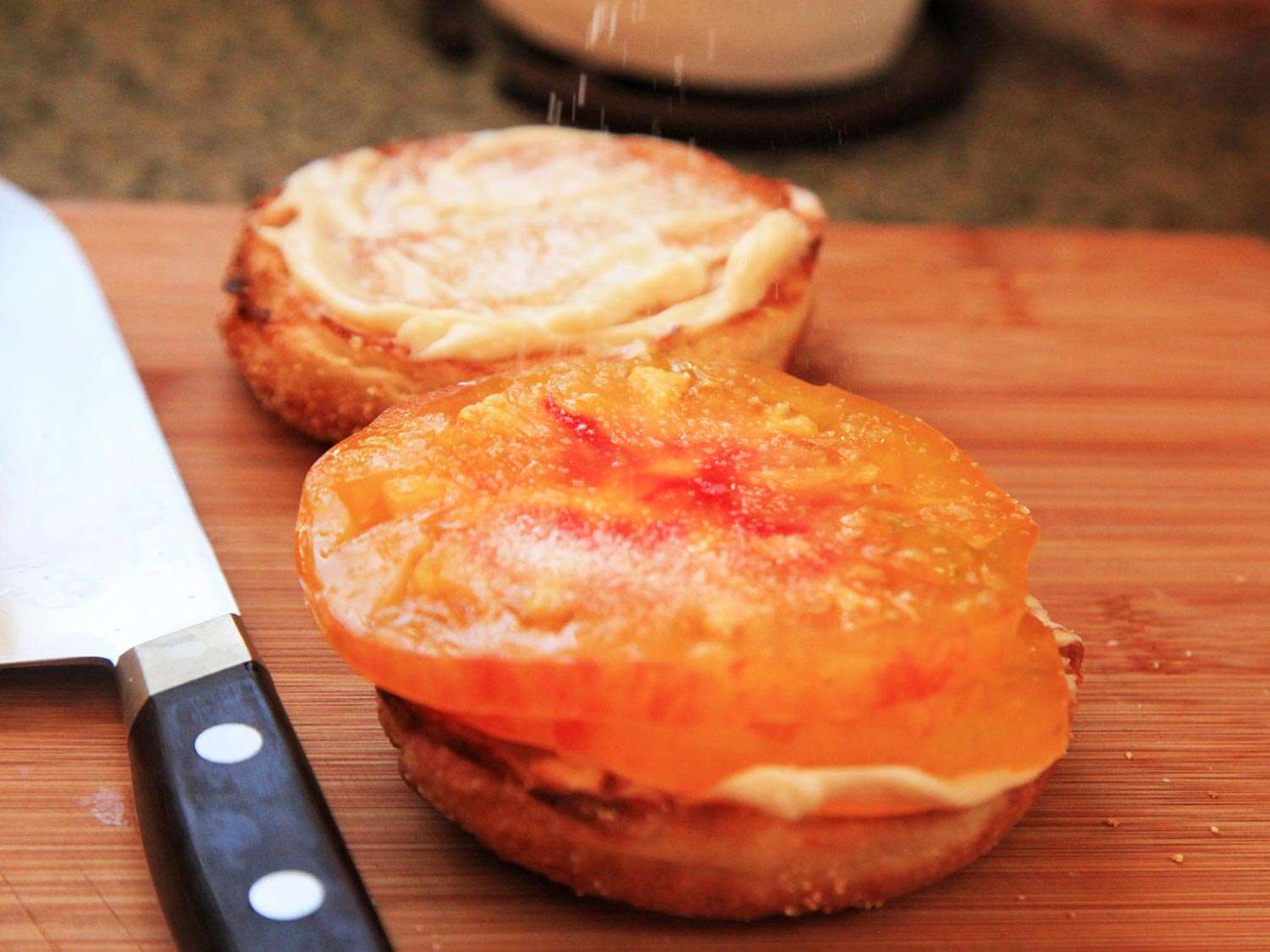 Salting tomato slices laid on top of a toasted English muffin spread with mayo