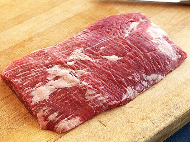 Large piece of raw flank steak resting on wooden cutting board