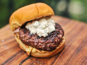 Closeup of a grilled burger topped with chunky blue cheese sauce.