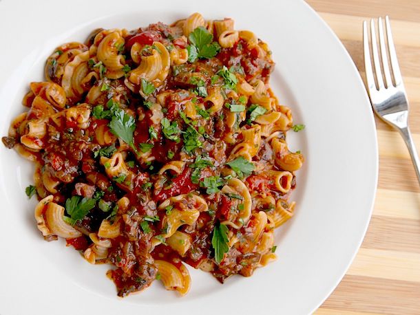 Overhead view of mushroom Bolognese tossed with crestos de gallos pasta, served in a shallow white bowl.