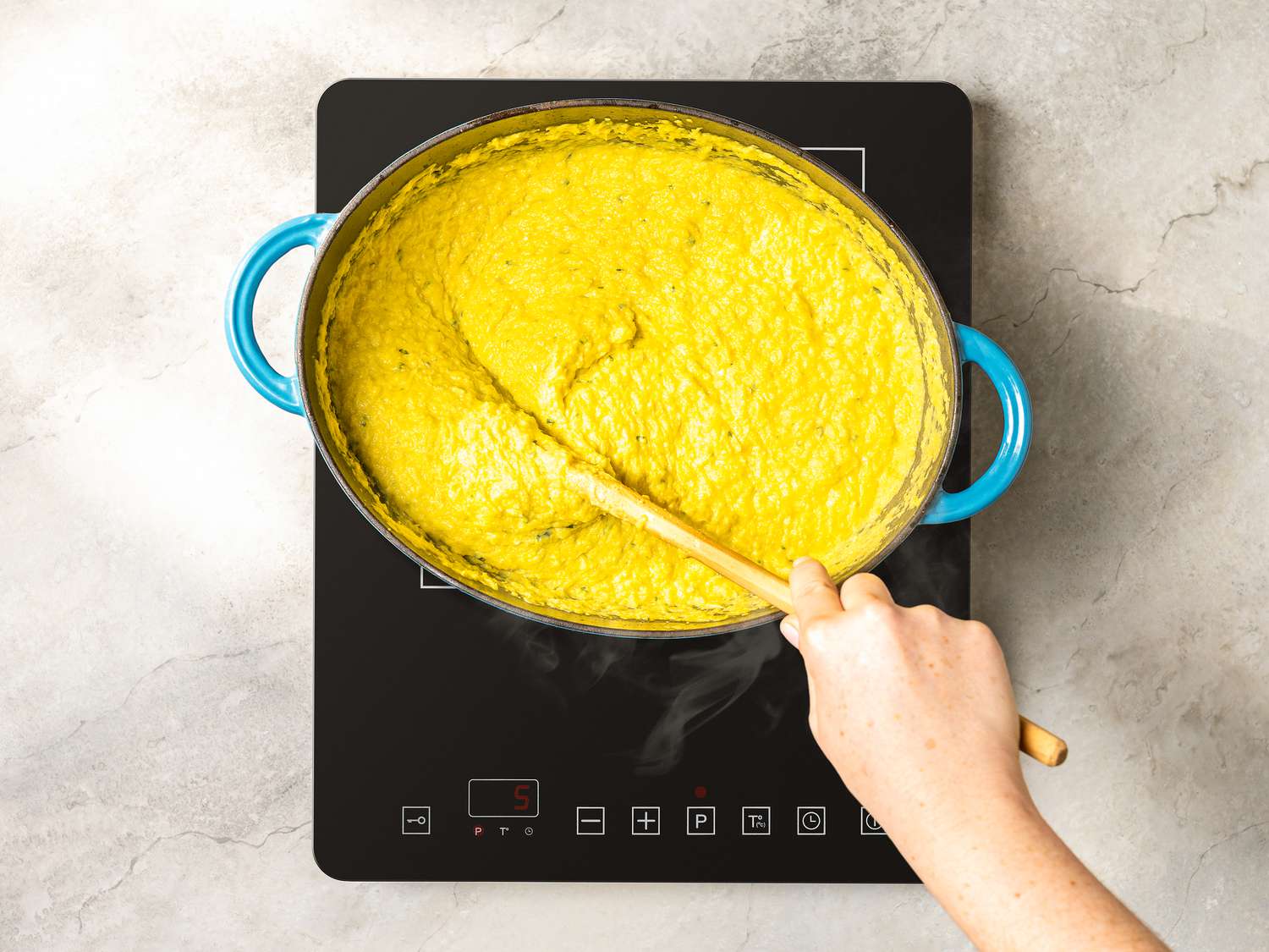 Puree of corn, and butter cooking and being mixed in a blue pot