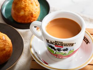 Cup of milk tea in a logoed mug on a plate with baked goods in the background