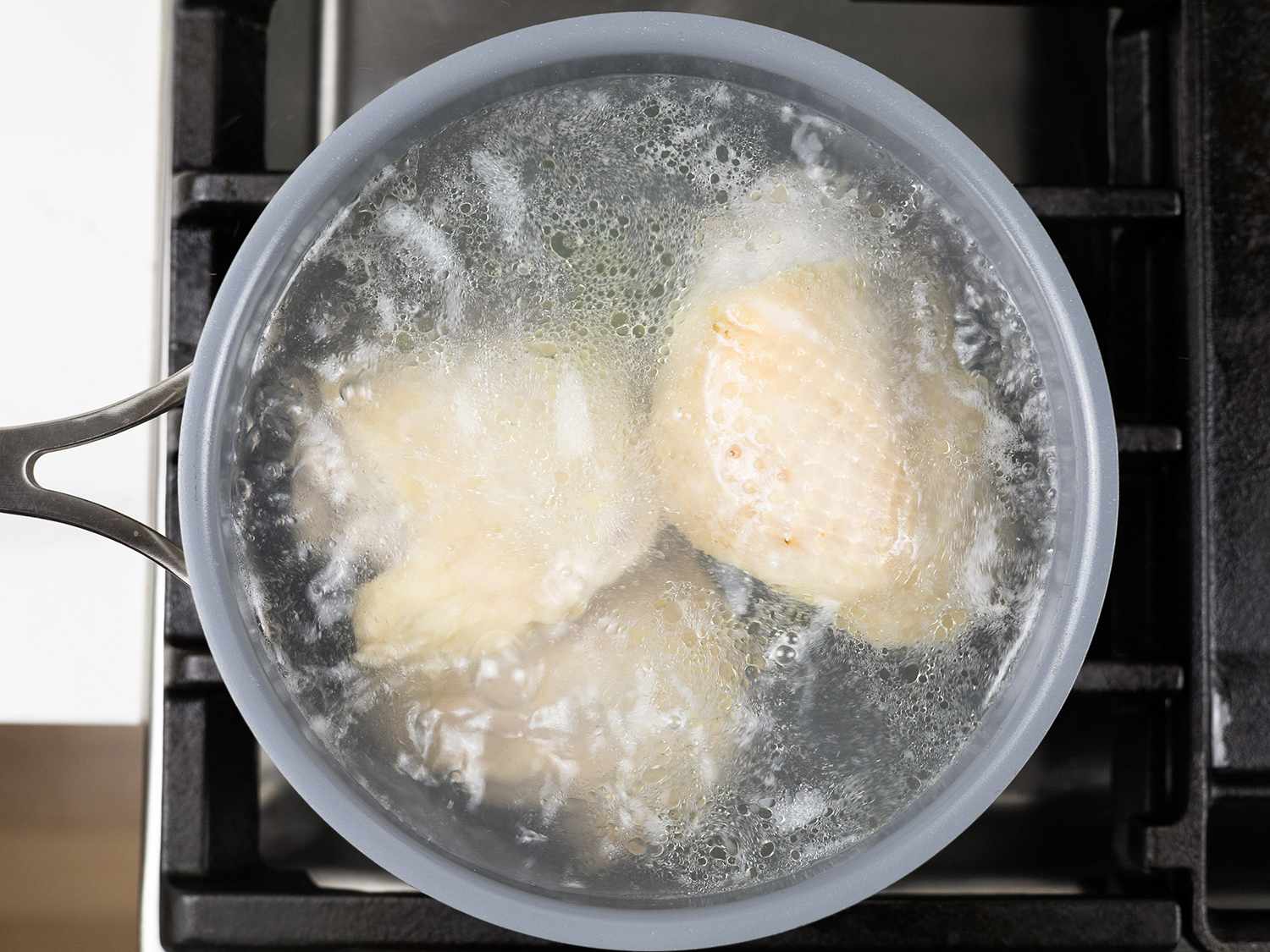 Overhead view of chicken thighs simmering in a saucepan.