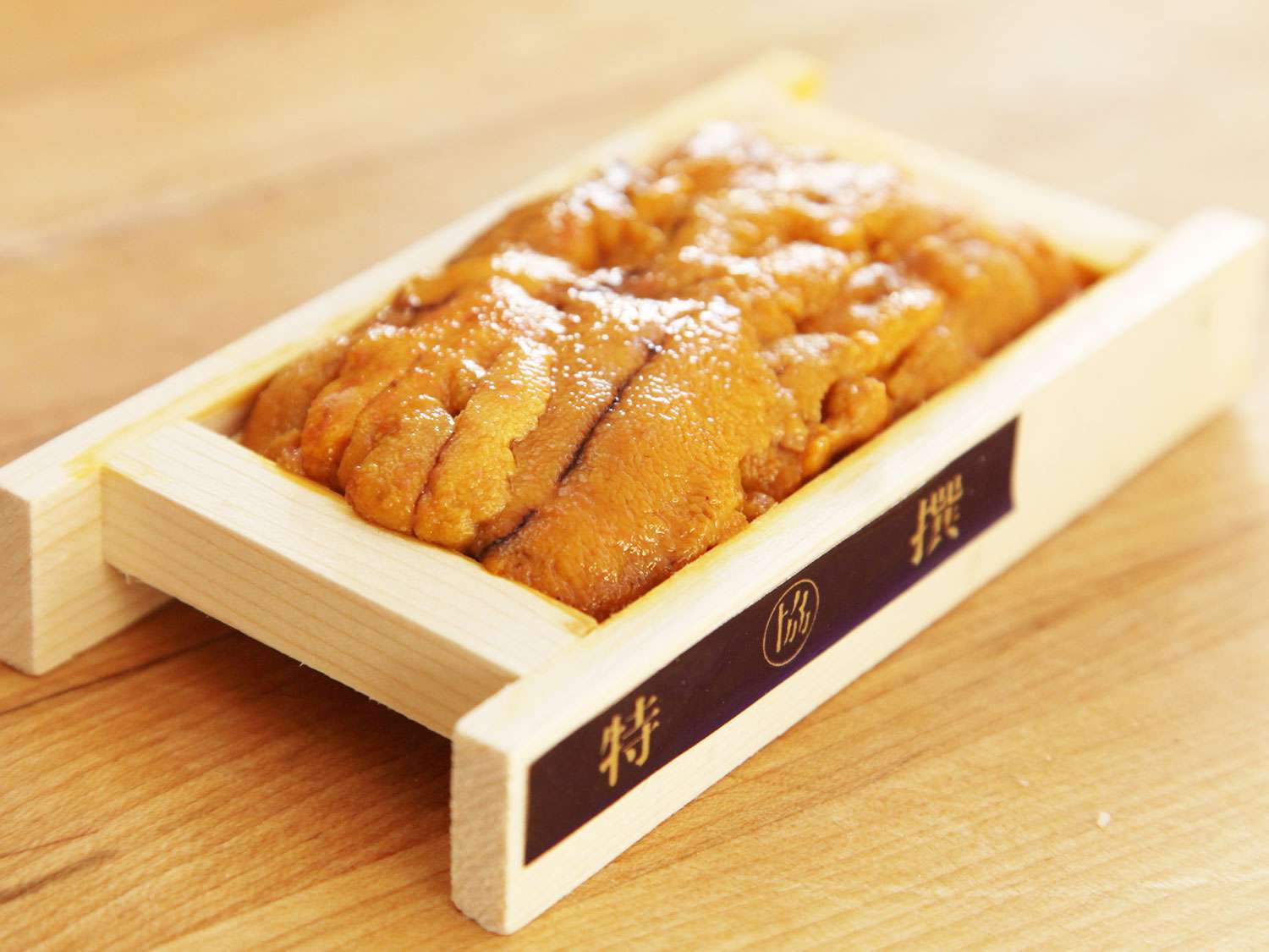 A wooden tray of fresh orange uni (sea urchin roe) on a wooden surface.
