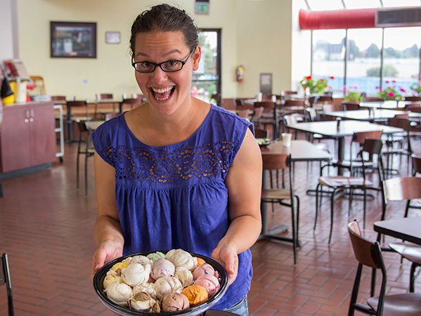 A woman holding a round plate filled with scoops of different flavors of ice cream. The woman has an ecstatic smile on her face.