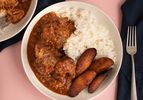 Rabo encendido with white rice and maduros served in a white bowl on a pink countertop.