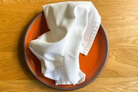 A folded cloth napkin on an orange ceramic plate