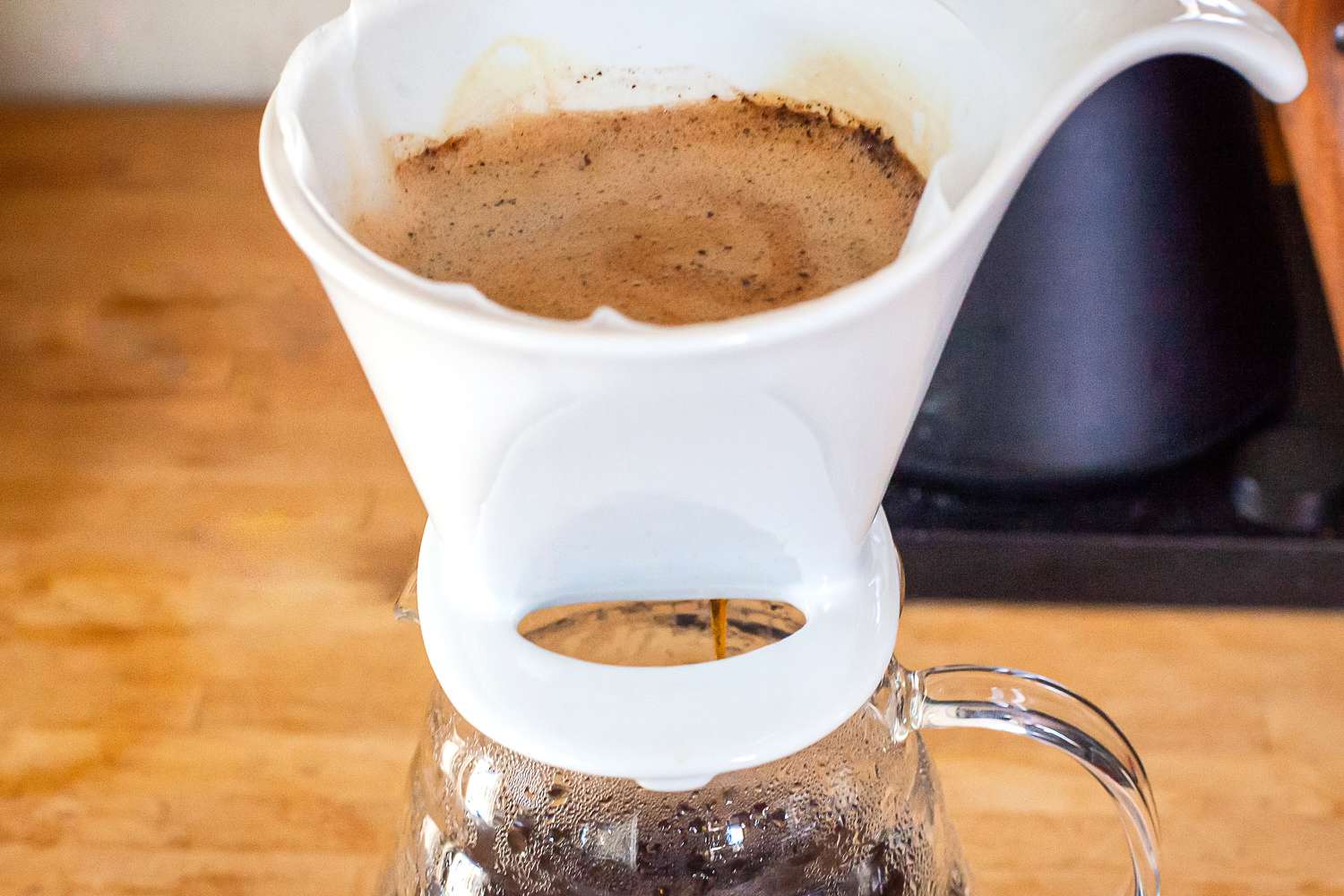 Pour-over coffee brewing in a white dripper placed atop a glass carafe.