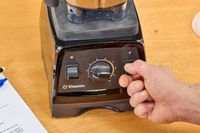 A close-up of a hand flipping a switch on the Vitamix 7500