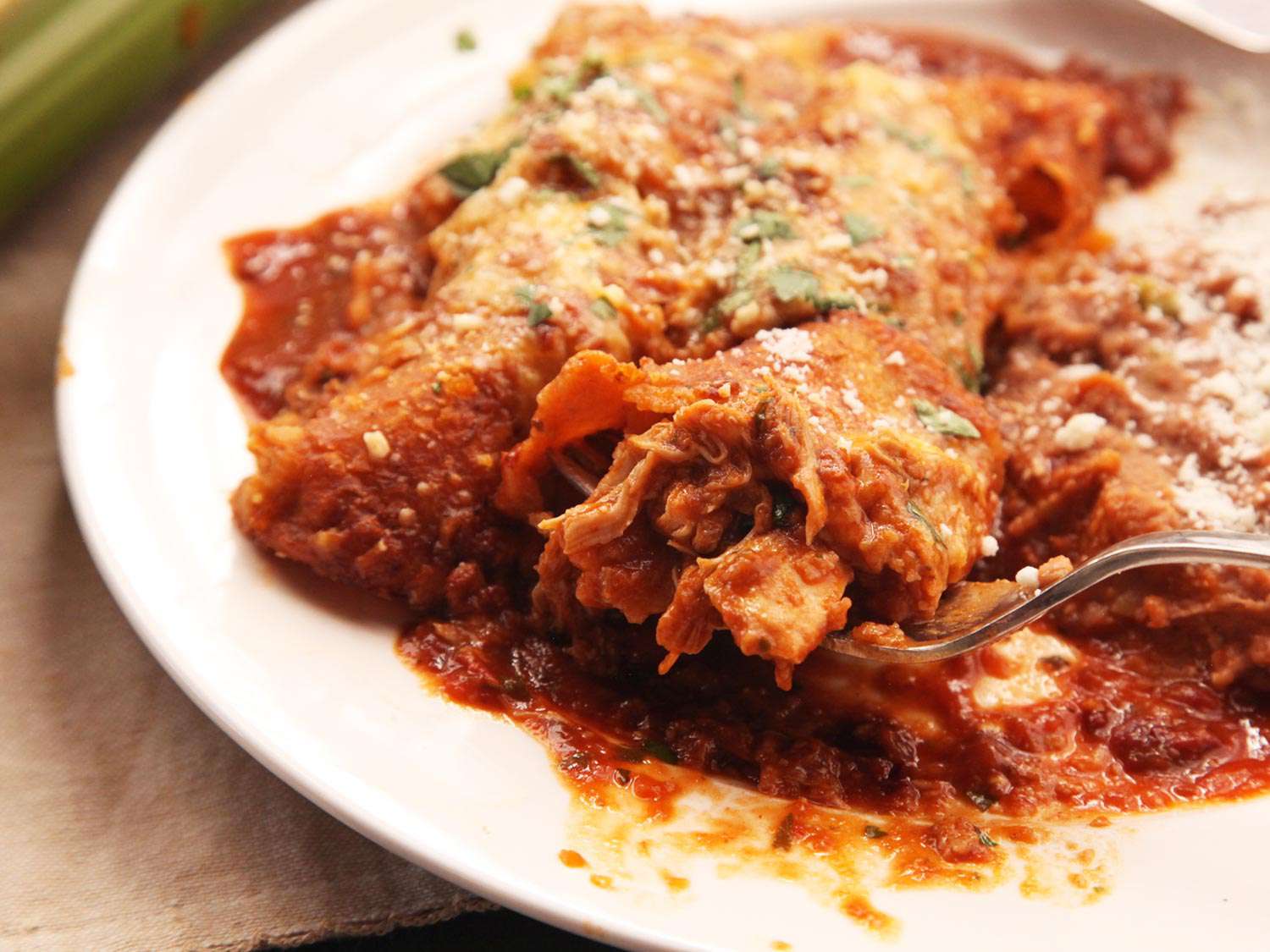 Close-up of a fork trying to make some headway into a big, messy helping of enchiladas.
