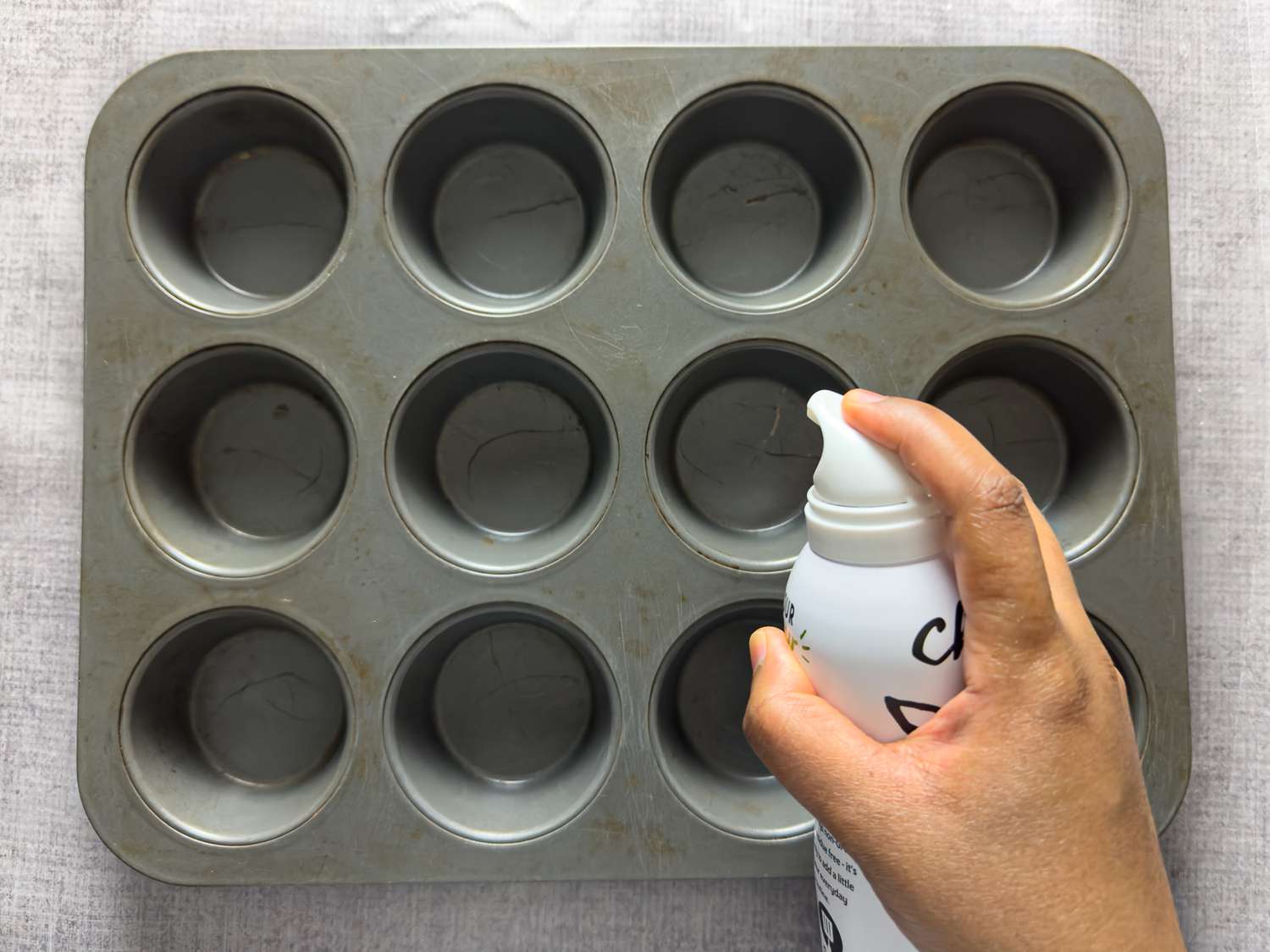 Spraying oil on muffin pan 