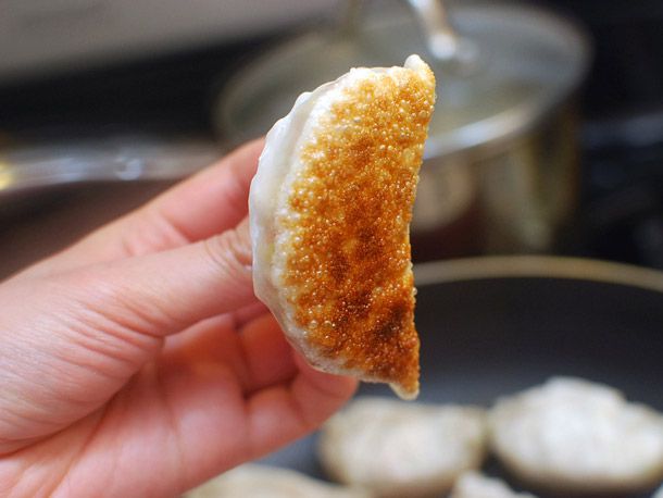 Hand holding a crispy-bottomed pan-fried vegetable dumpling.