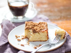 A piece of coffee cake on a serving plate; a fork has taken a corner of the cake out of it. 