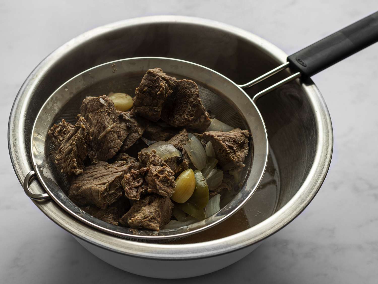 Straining beef mixture through a fine-mesh strainer set over a large heat proof bowl.