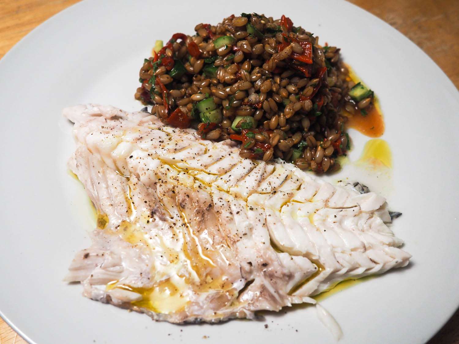 A piece of Whole Roasted Fish With Oregano, Parsley, and Lemon on a white plate, served with a lentil salad. 