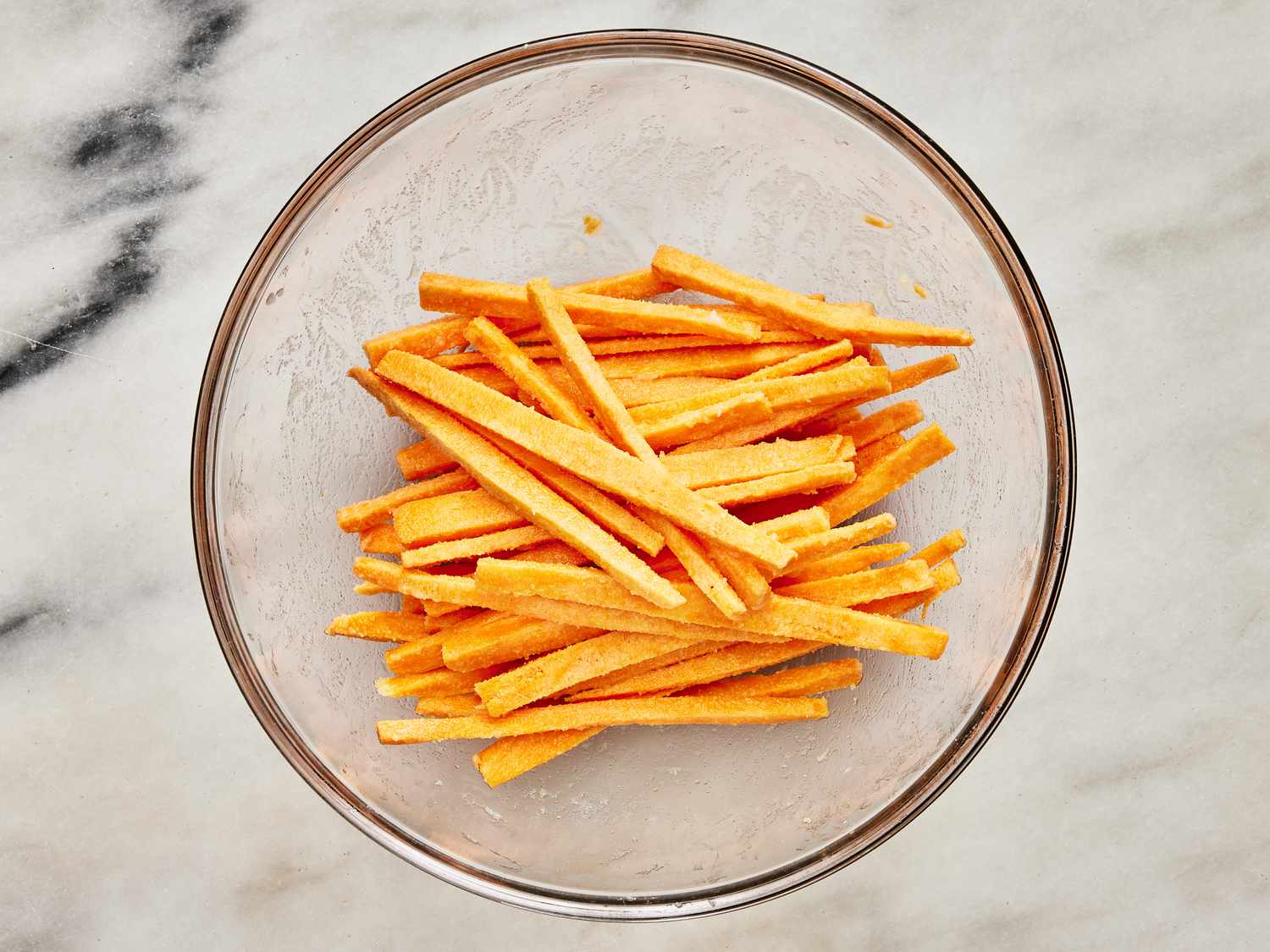 Glass bowl with slices of sweet potatoes tossed and coated evenly.