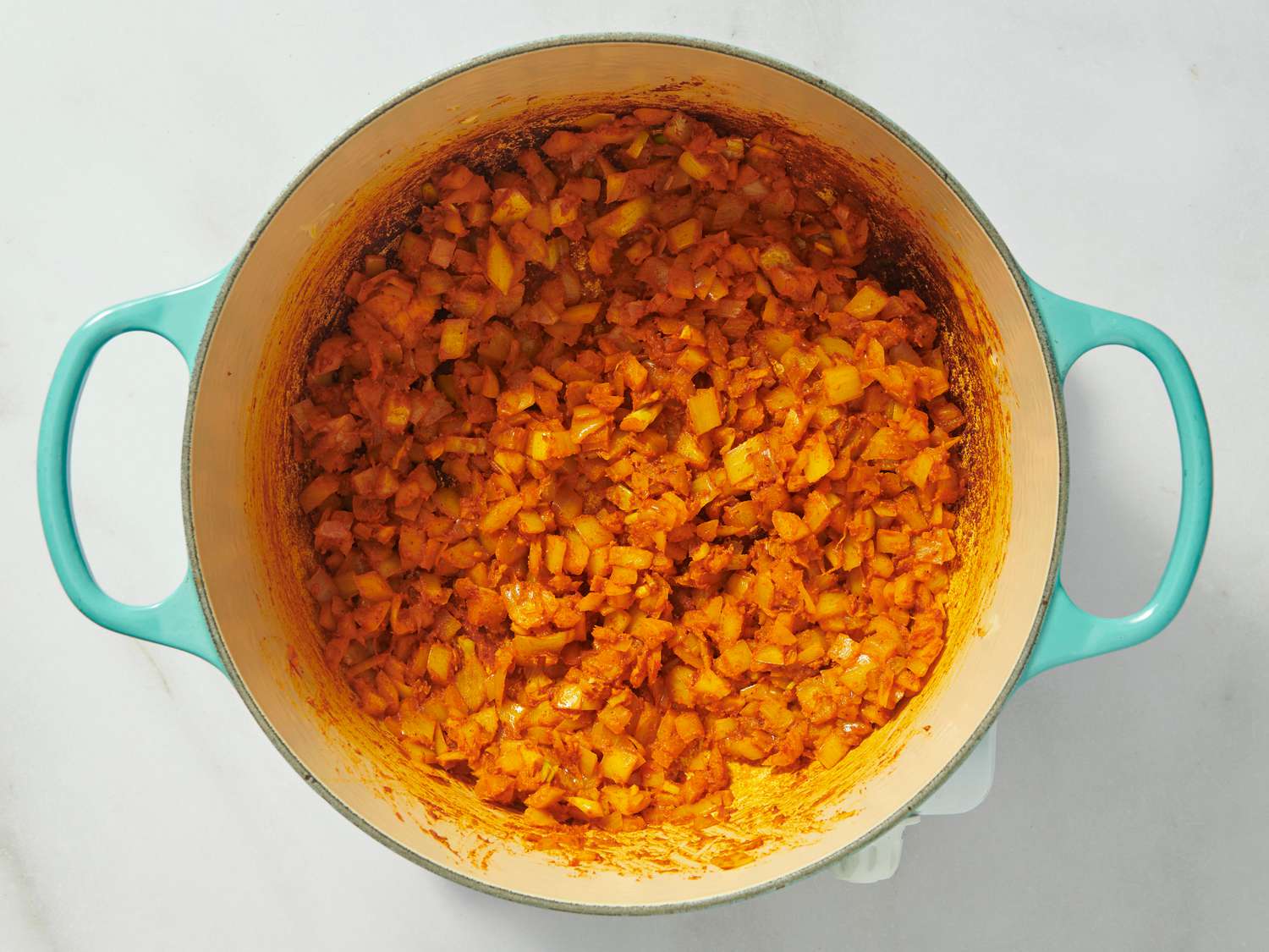 onion, garlic and spices cooking in dutch oven on white surface 