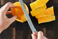 A serrated knife cuts through a butternut squash.