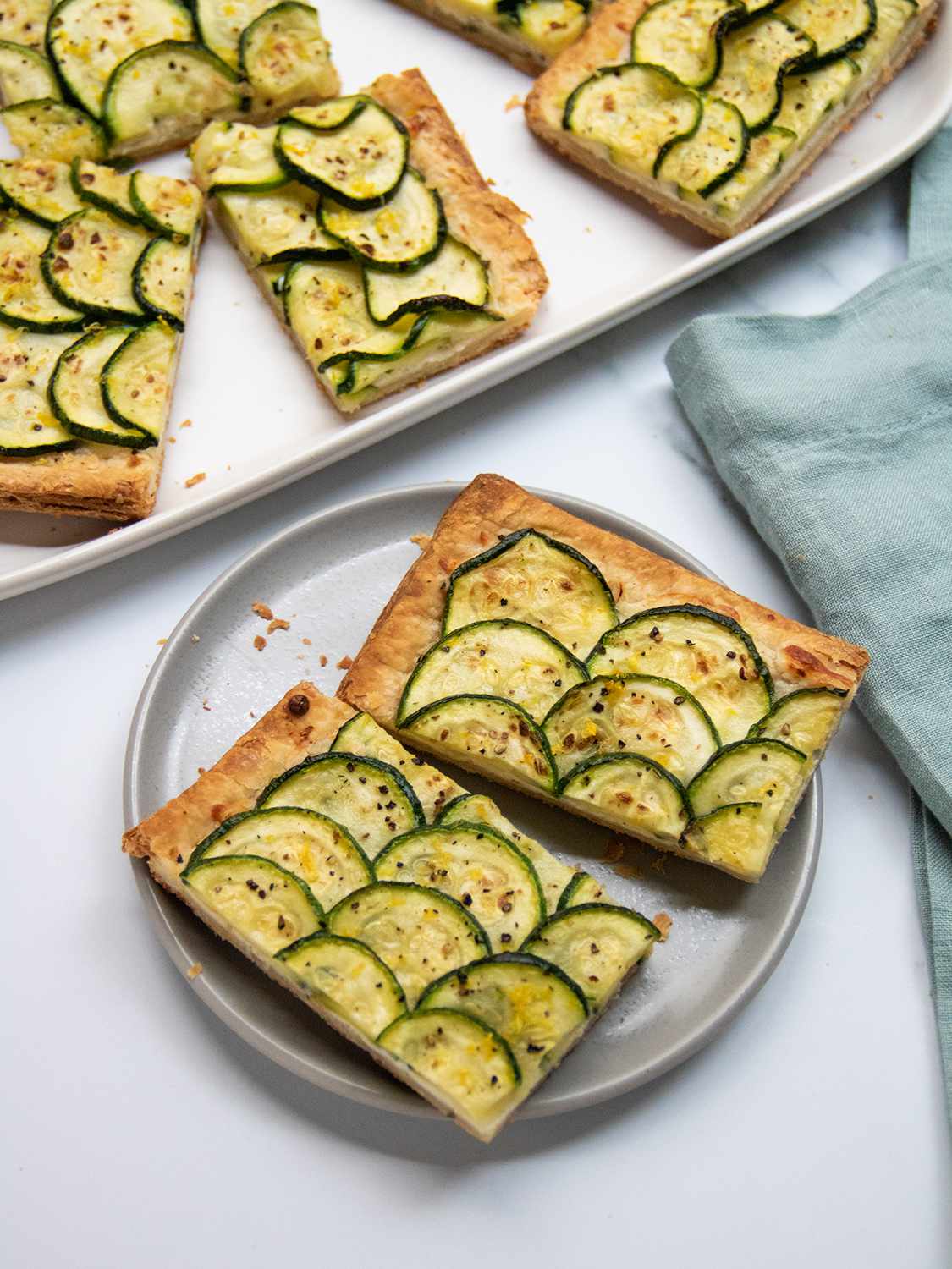 Cut slices of zucchini tart on a plate next to a rimmed baking sheet with remaining tart slices